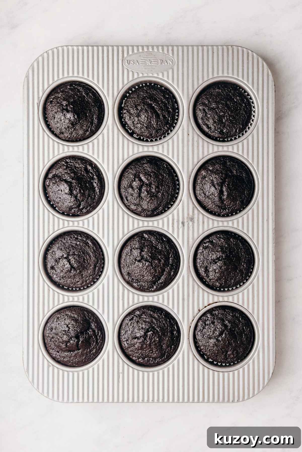 Baked chocolate cupcakes with cupcake liners in a metal cupcake tin on a grey marbled background.