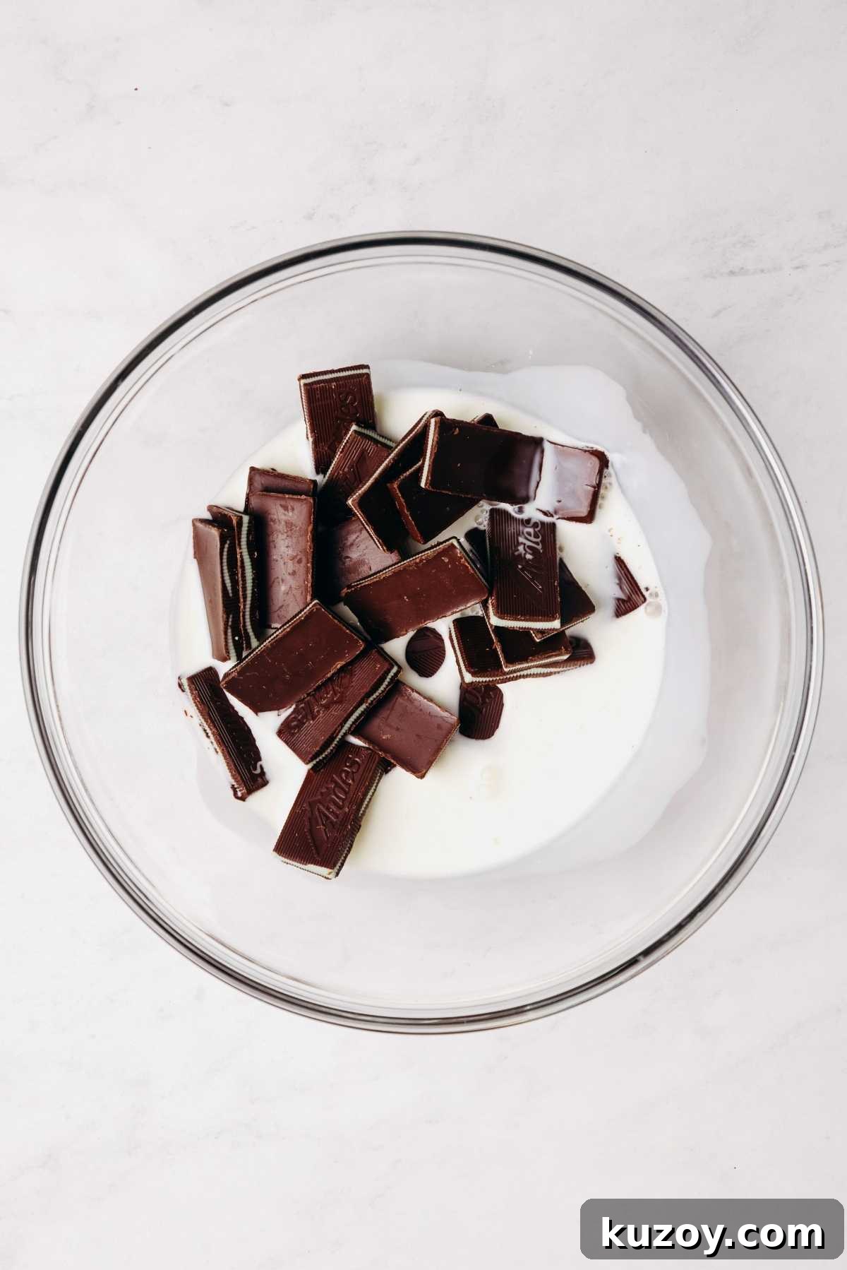 Andes mint chocolates and heavy cream in a small glass mixing bowl on a grey marbled background.