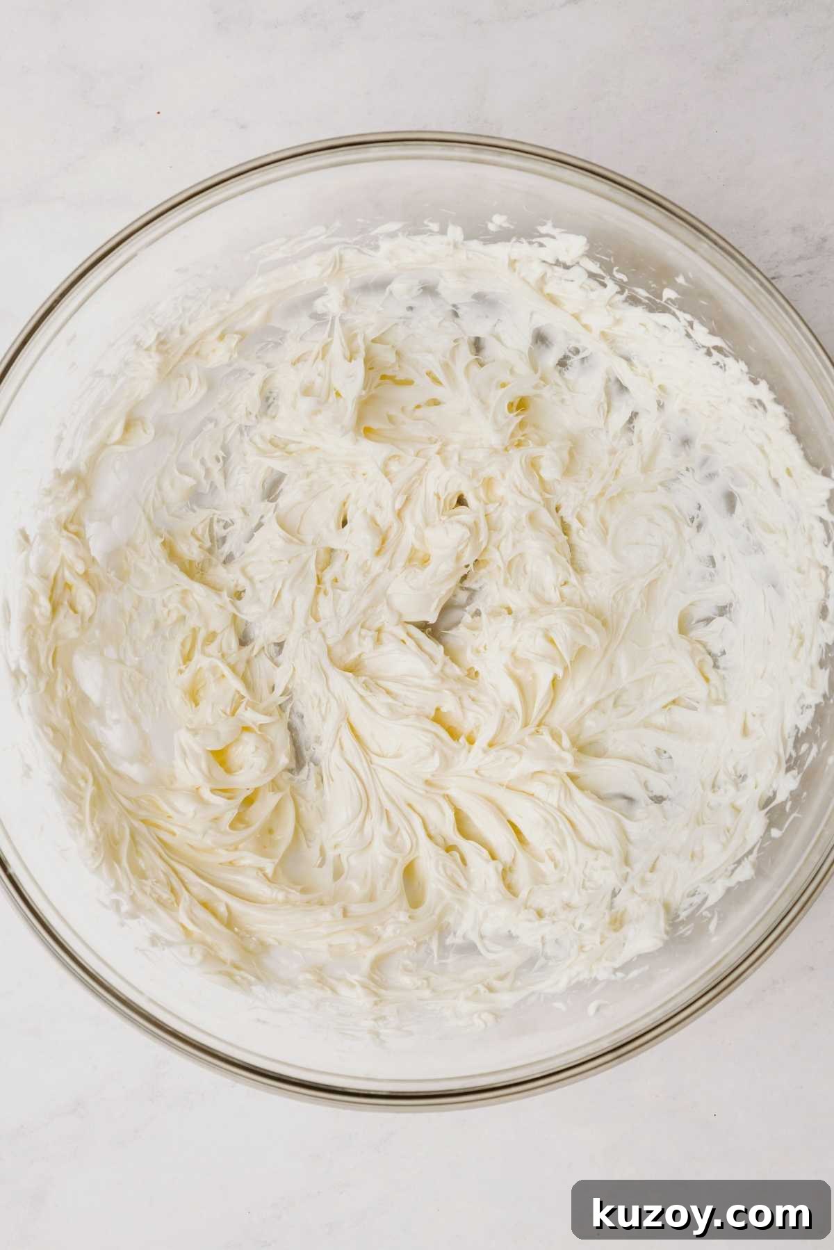 Whisked unsalted butter in a large glass mixing bowl on a grey marbled background.