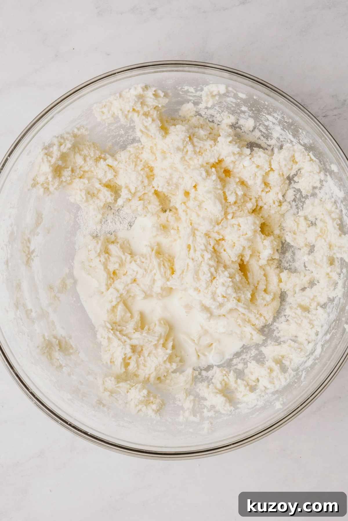 Powdered sugar and peppermint extract whisked together with unsalted butter in large glass mixing bowl on a grey marbled background.