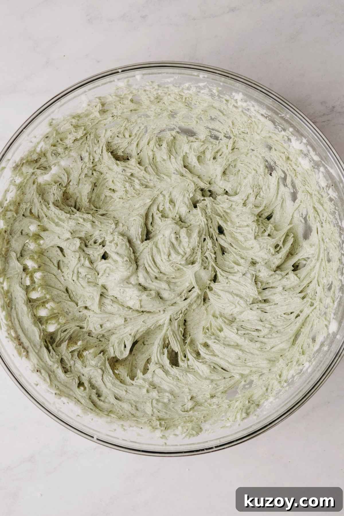 Mint chocolate oreo buttercream frosting in a large glass mixing bowl on a grey marbled background.