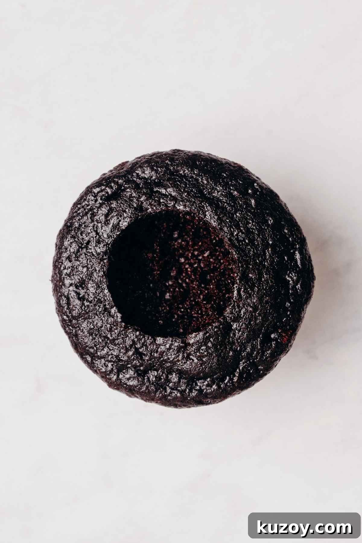 One chocolate cupcake with cored out center on a grey marbled background.