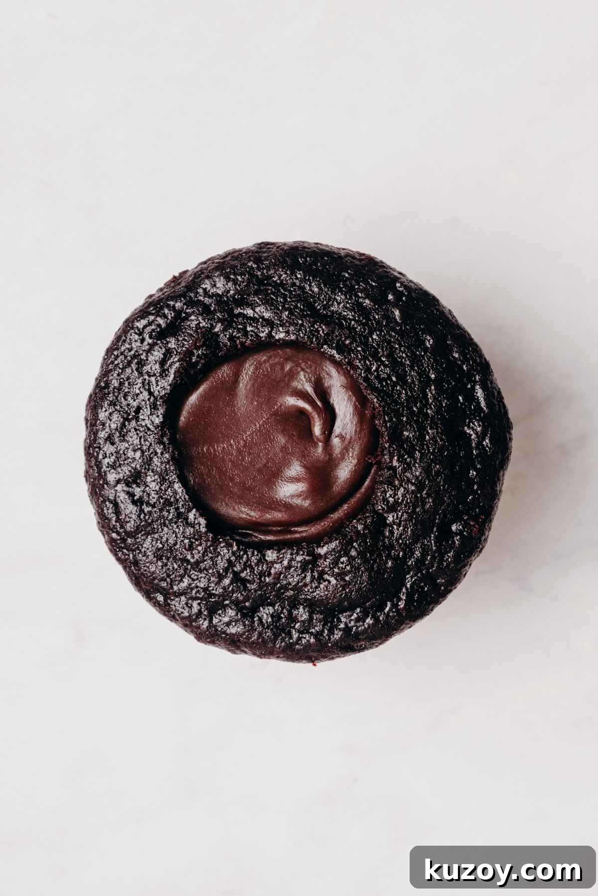 One chocolate cupcake with cored out center filled with mint chocolate ganache on a grey marbled background.
