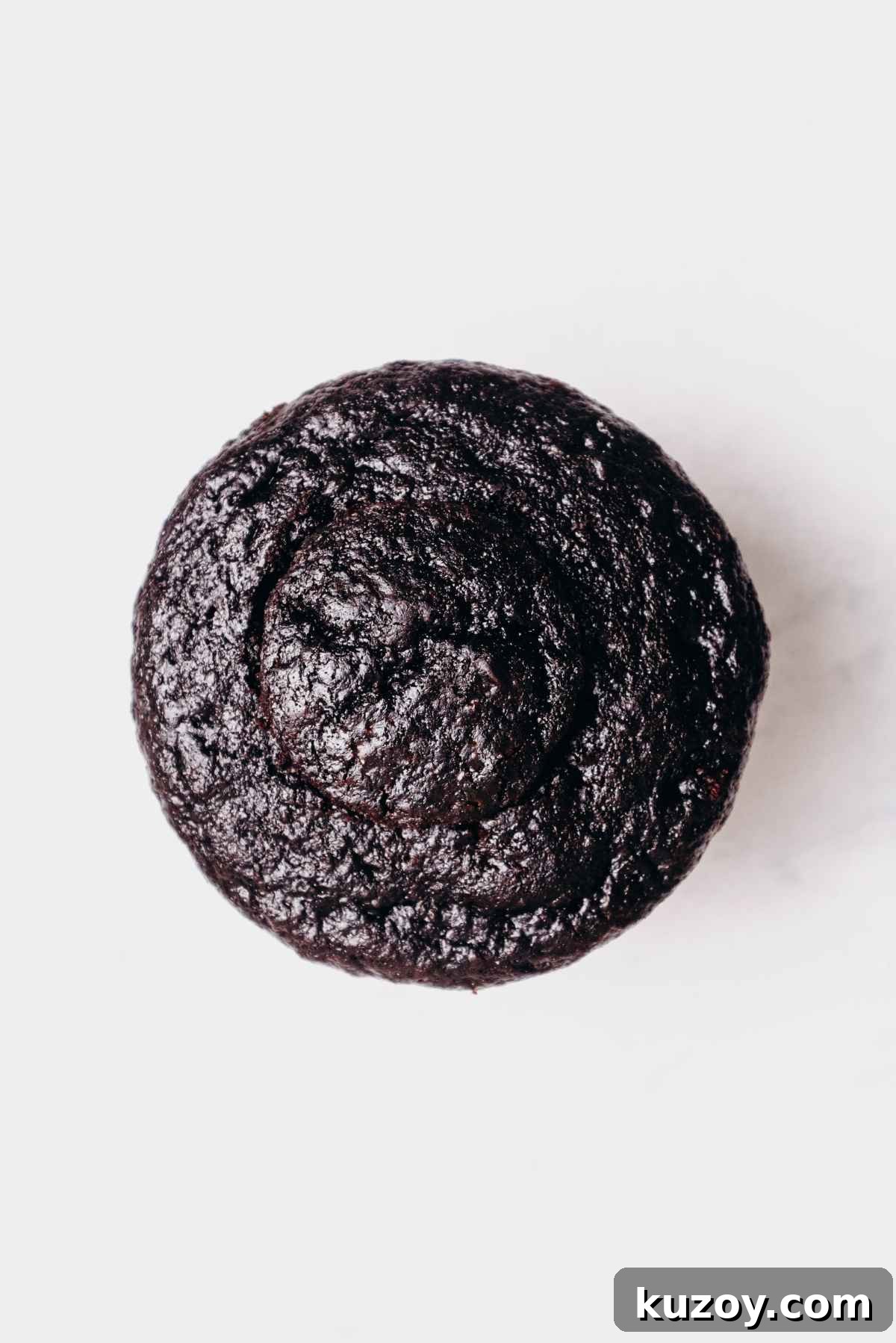 One chocolate cupcake filled with mint chocolate ganache topped with round piece of chocolate cupcake on a grey marbled background.