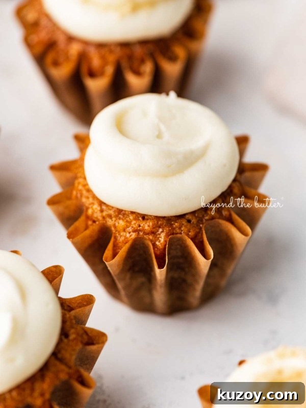 Super moist carrot cake cupcakes topped with cream cheese frosting on a white background.