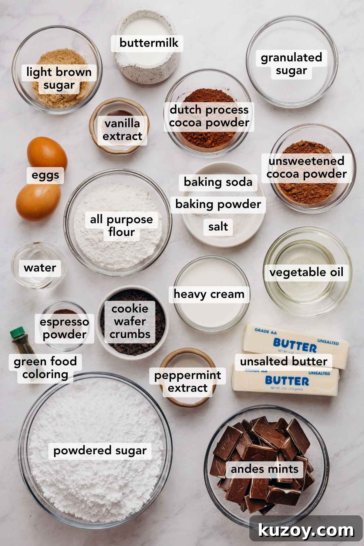 Ingredients in various size bowls labeled as light brown sugar, buttermilk, dutch process cocoa powder, unsweetened cocoa powder, granulated sugar, eggs, vanilla extract, baking soda, baking powder, salt, all purpose flour, water, heavy cream, vegetable oil, espresso powder, chocolate wafer crumbs, peppermint extract, green food coloring, unsalted butter, powdered sugar, and andes mints on a white marbled background.