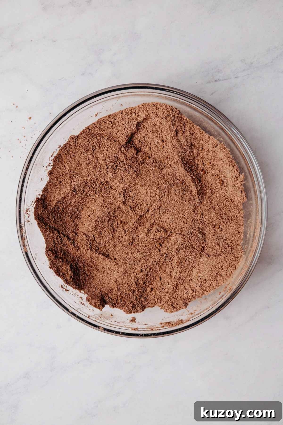 Whisked all purpose flour, granulated sugar, light brown sugar, dutch process cocoa powder, unsweetened cocoa powder, baking powder, baking soda, and salt in a medium size glass mixing bowl on a grey marbled background.