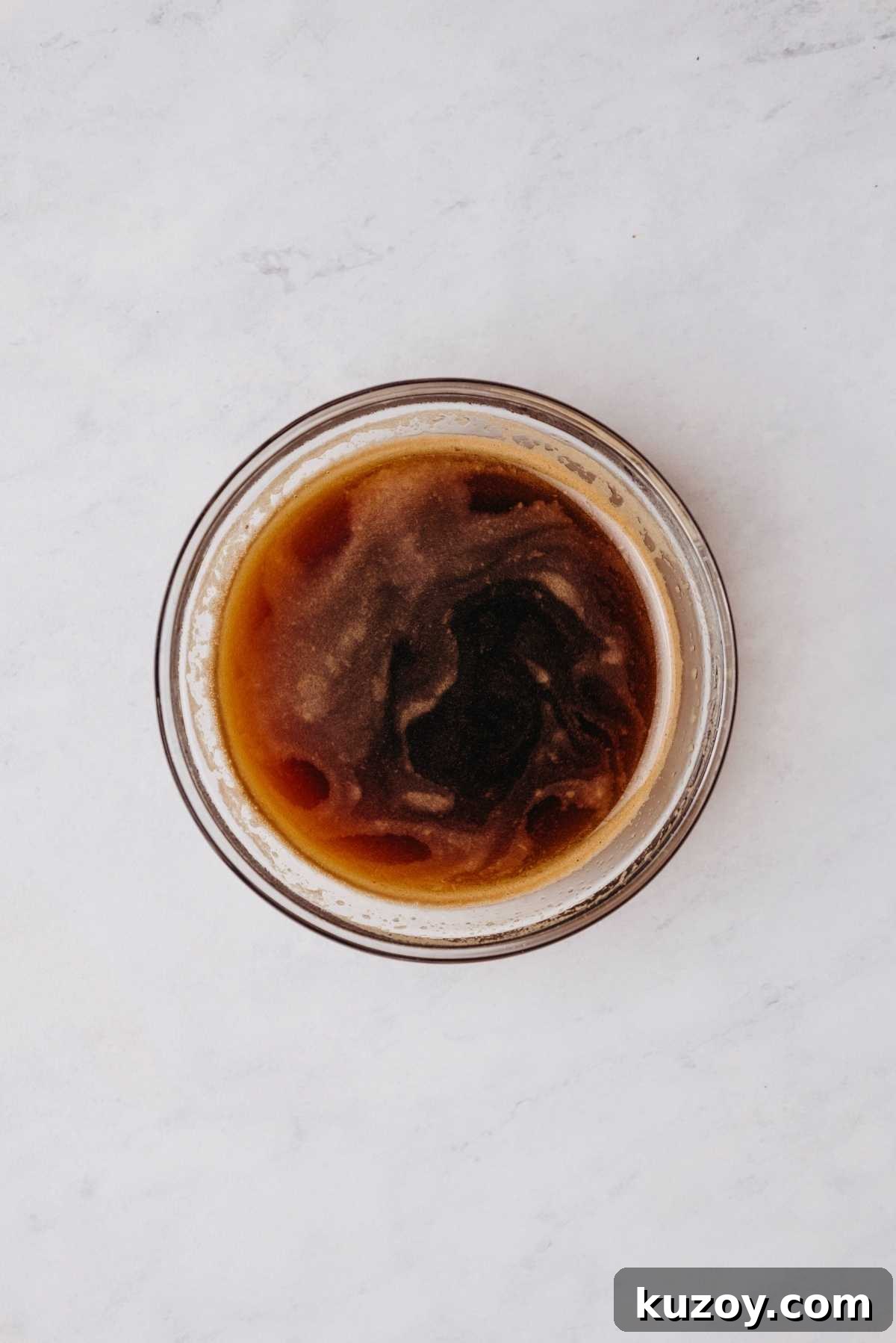 Espresso powder and hot water whisked together in a small glass mixing bowl on a grey marbled background.