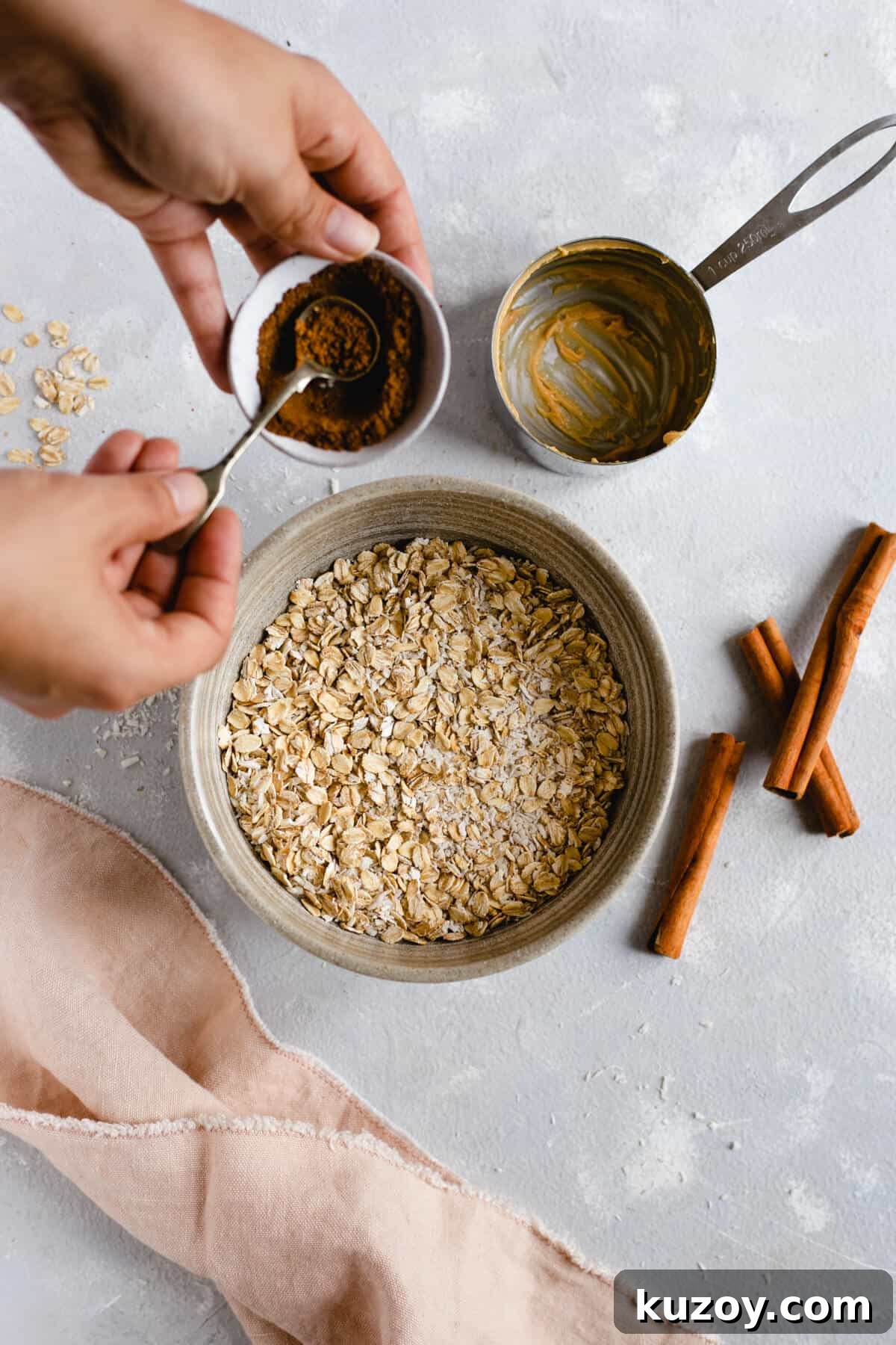 Coconut Peanut Butter Energy Bites with Warm Spices 3 Overhead shot of bowl with oats and shredded coconut with someone adding mixed spice to the mixture