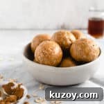 A straight-on angle shot of small bowl filled with coconut and peanut butter spiced energy bites with small jar of maple syrup in the background