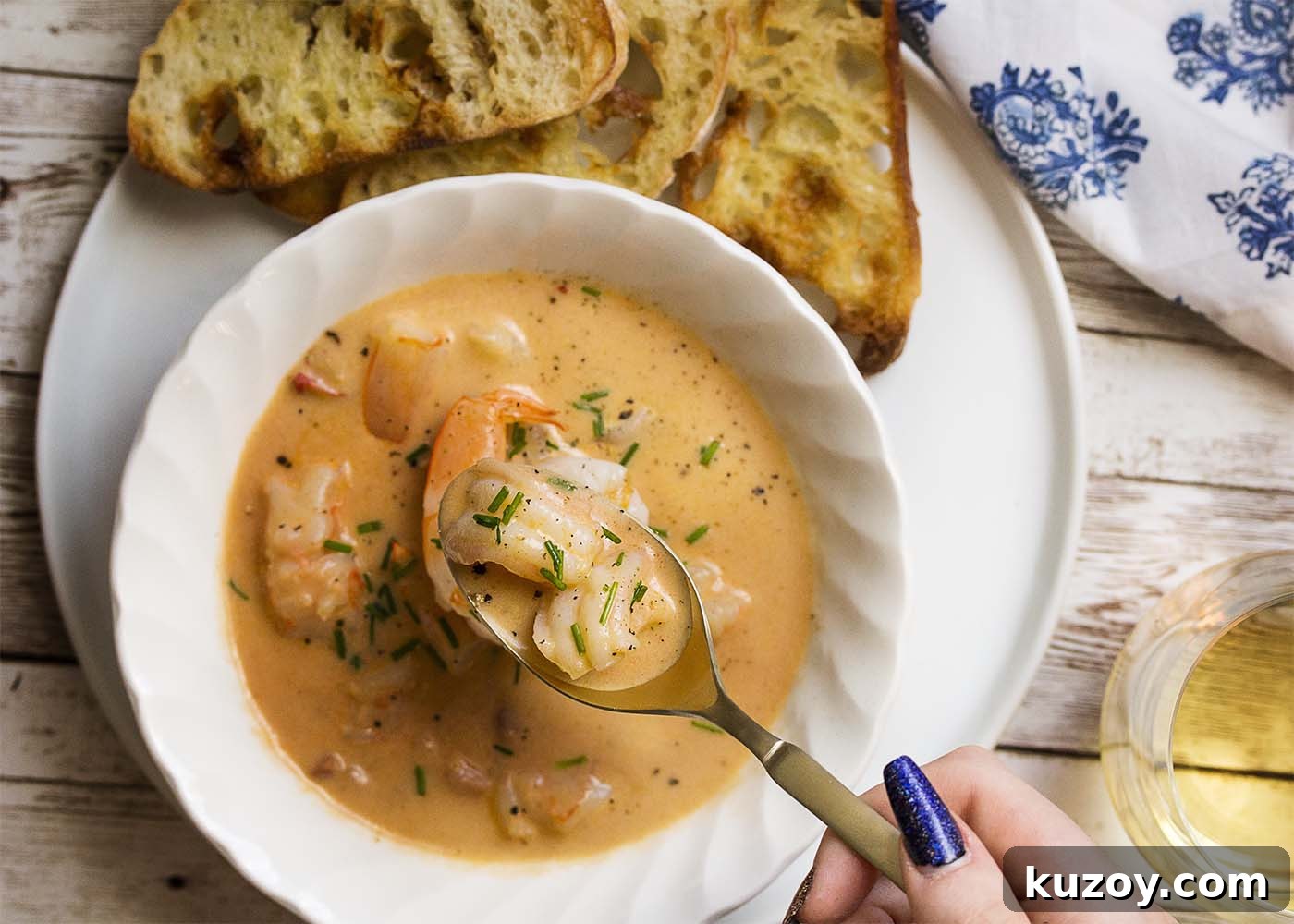 Learn how to make the best creamy shrimp bisque! This easy French recipe features a rich stock using the shells, tomato paste, and a bit of bourbon to create a wonderfully complex soup. | justalittlebitofbacon.com #shrimprecipes #seafoodrecipes #souprecipes #frenchfood #shrimp #bisque #french Top view of a bowl of thick creamy shrimp soup. A filled spoon held above the bowl.