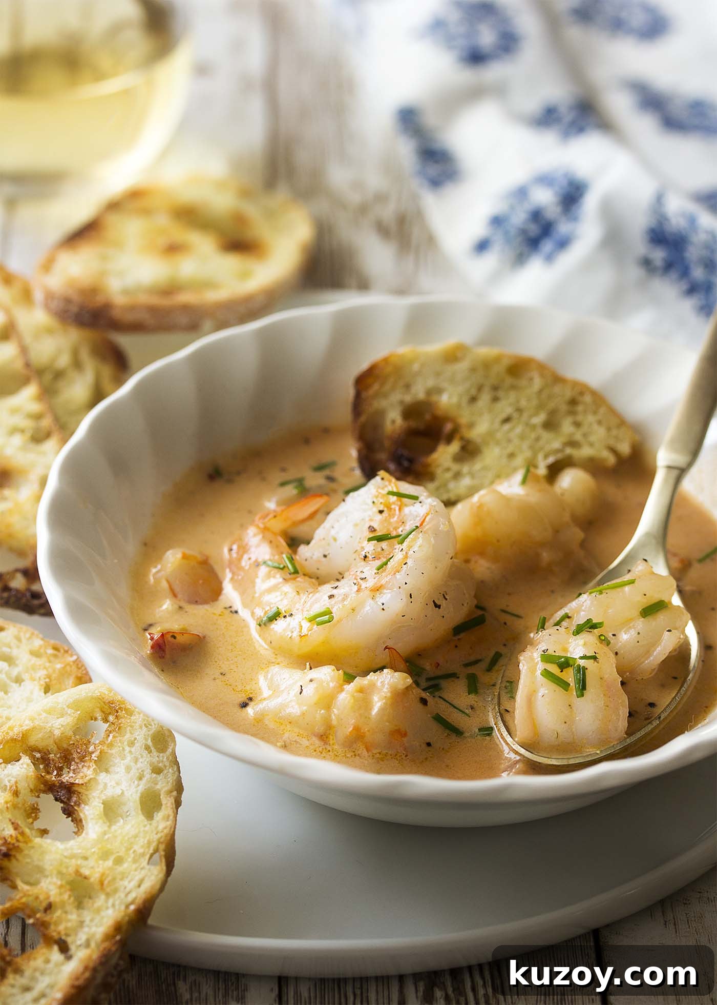 Learn how to make the best creamy shrimp bisque! This easy French recipe features a rich stock using the shells, tomato paste, and a bit of bourbon to create a wonderfully complex soup. | justalittlebitofbacon.com #shrimprecipes #seafoodrecipes #souprecipes #frenchfood #shrimp #bisque #french Creamy soup in a white bowl on a plate. Pieces of shrimp in the spoon.