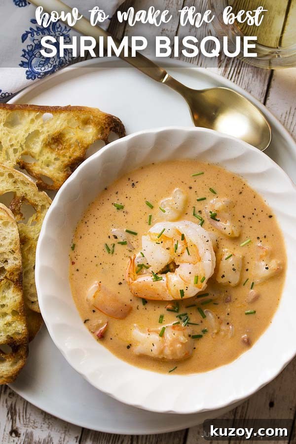 Learn how to make the best creamy shrimp bisque! This easy French recipe features a rich stock using the shells, tomato paste, and a bit of bourbon to create a wonderfully complex soup. | justalittlebitofbacon.com #shrimprecipes #seafoodrecipes #souprecipes #frenchfood #shrimp #bisque #french Soup in a white bowl on a plate with text overlay - Shrimp Bisque.
