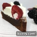 A slice of decorated brownie cake with blackberries on a white plate.