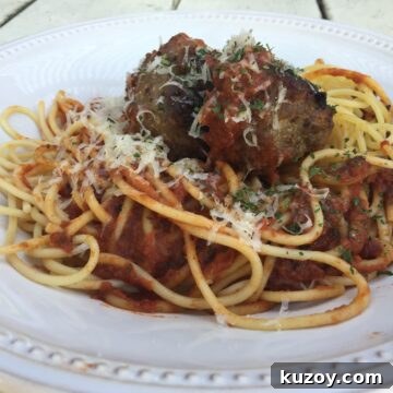 Meatballs on top spaghetti and sauce, with cheese garnish.