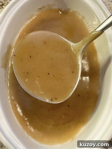 A gravy bowl full of gravy with a serving spoon.