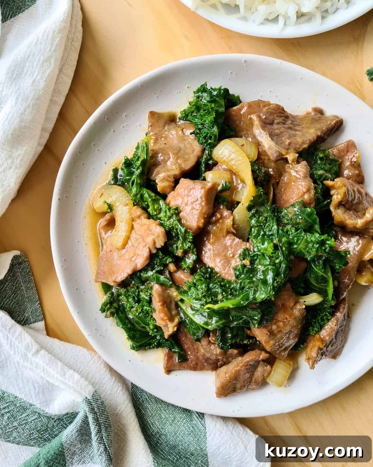 A large plate of ginger beef and kale with table cloth loosely place on its left