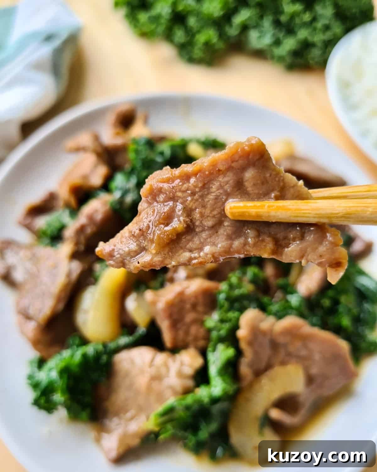 close up image of a piece of cooked, velvety beef slice held up by chopsticks