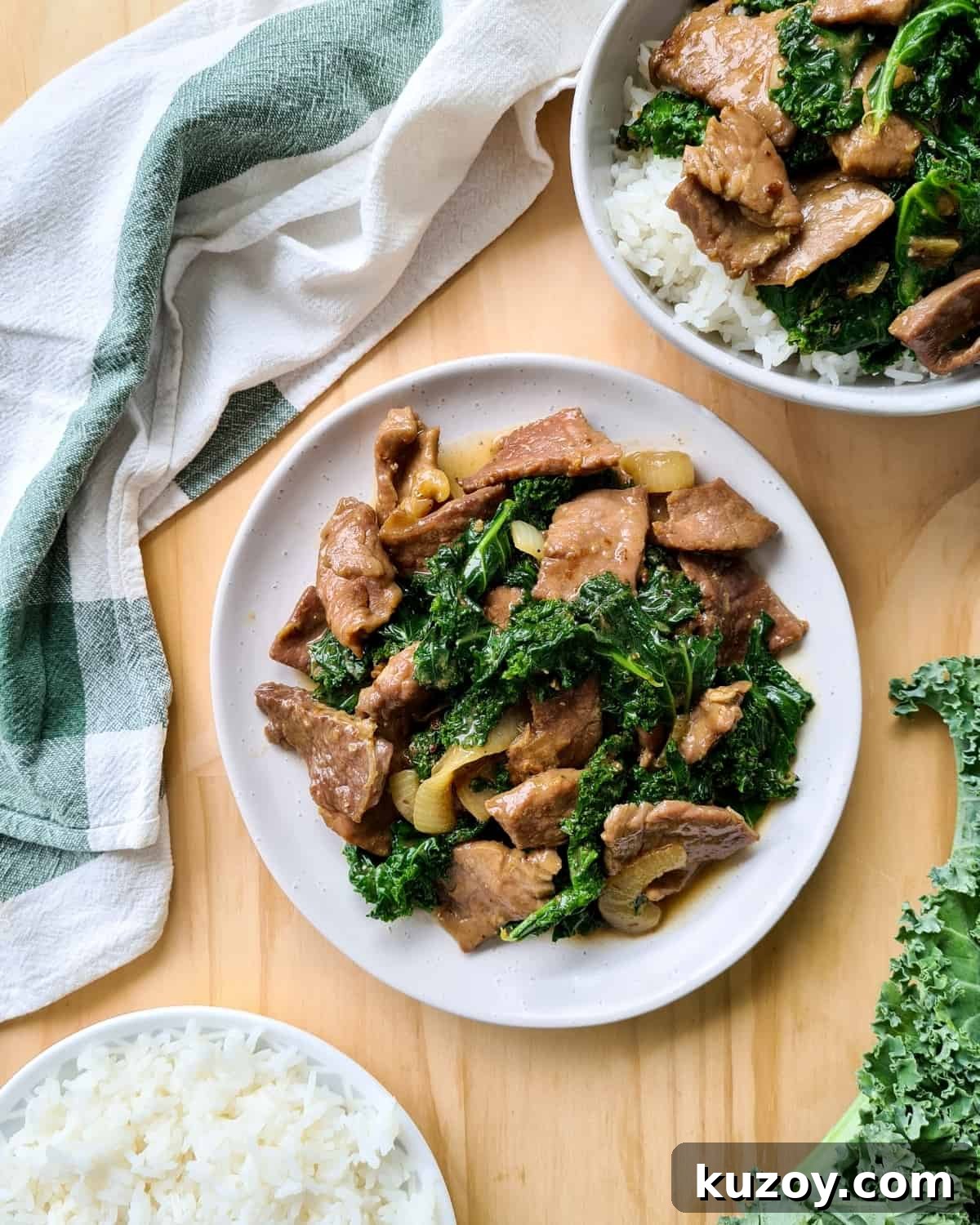 overhead shot of a plate of ginger beef and kale stir fry. Cooked rice in bottom left hand corner and top right hand corner a bowl of rice topped with ginger beef and kale.