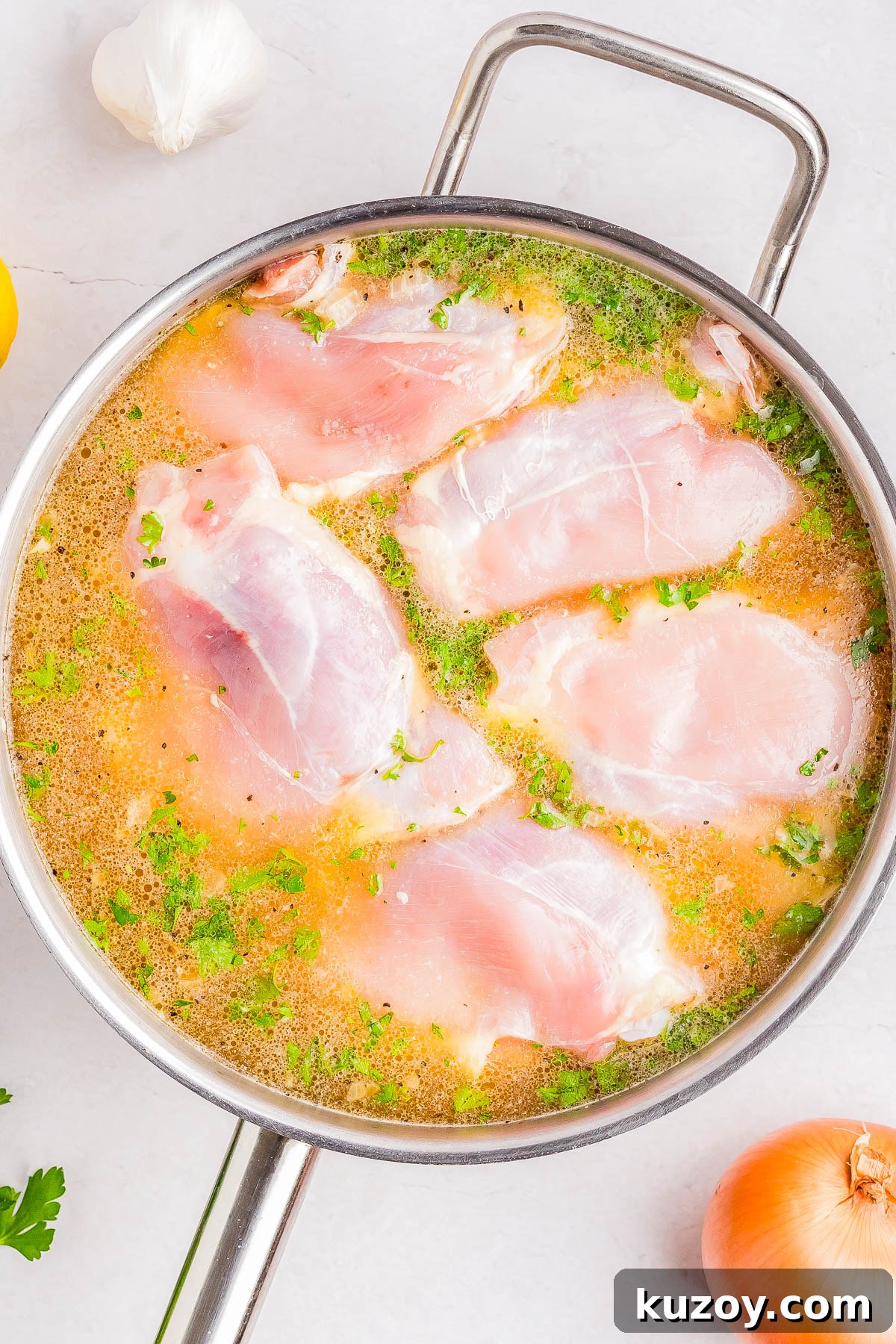 Raw chicken breasts marinating in a metal pan with a liquid containing herbs and spices.