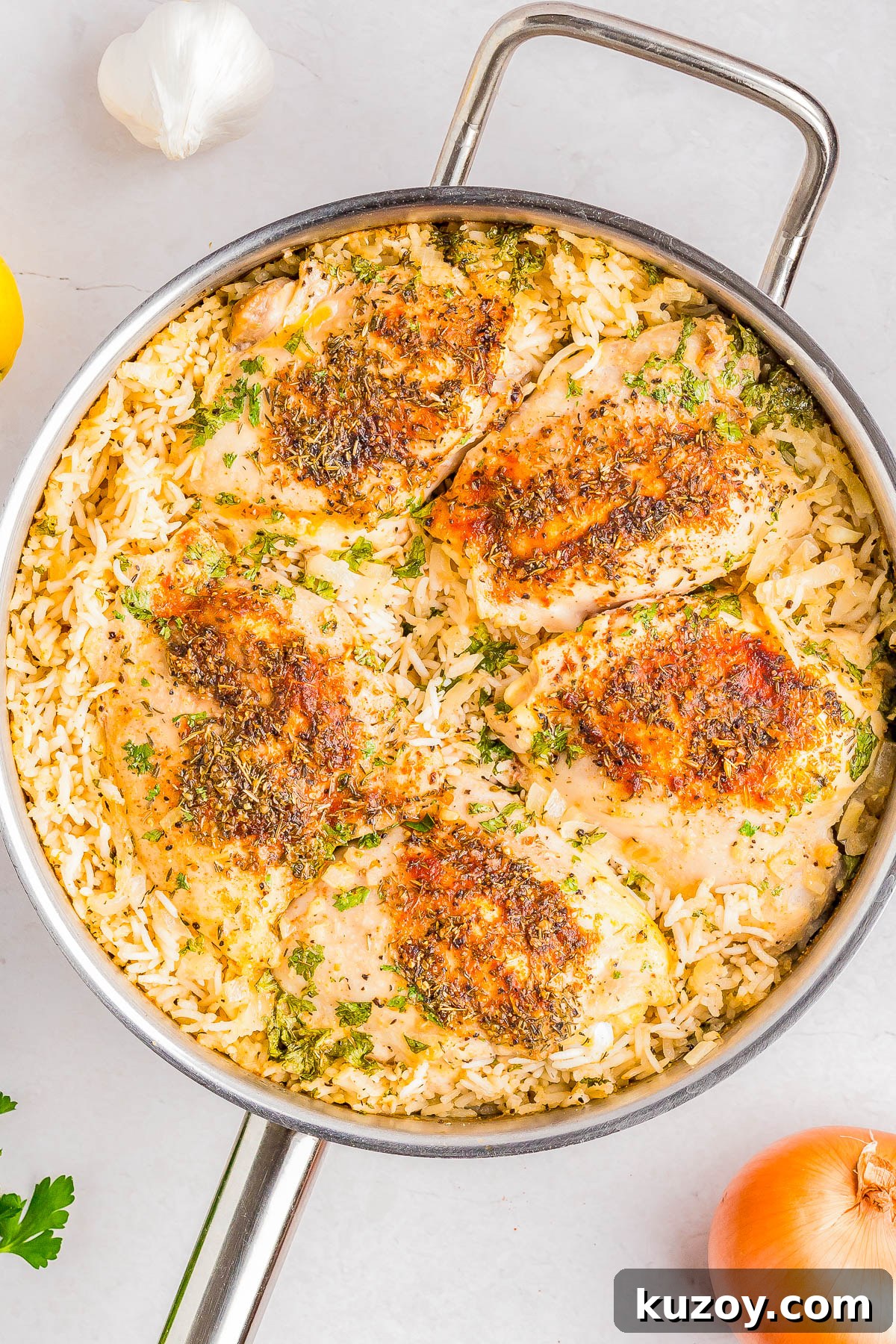 A skillet with cooked, seasoned chicken breasts on a bed of rice, garnished with herbs.