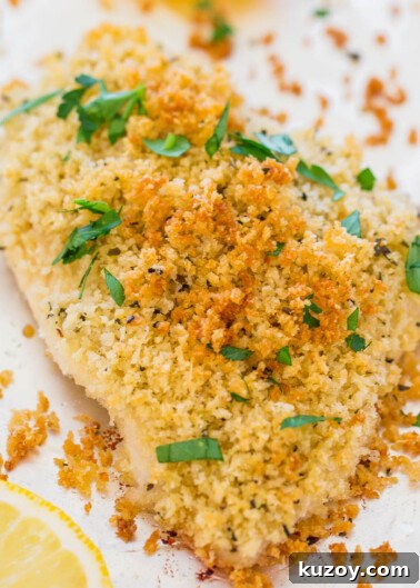 Breaded chicken breast garnished with parsley and lemon on a white background.
