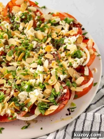A white plate with tomato feta herb almond salad on it.