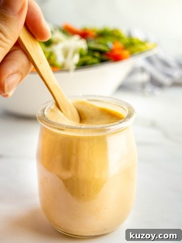 A glass jar with thick light brown dressing in it being stirred by a hand