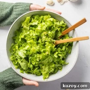 Toasted Garlic Salad with Crispy Garlic Dressing 15 A bowl of green salad with wooden spoons in it being held by a person wearing a green jumper.