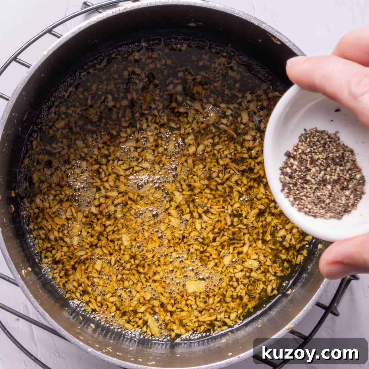 Toasted Garlic Salad with Crispy Garlic Dressing 5 A pan with toasted garlic in oil and a hand adding a small white bowl of black pepper to it.