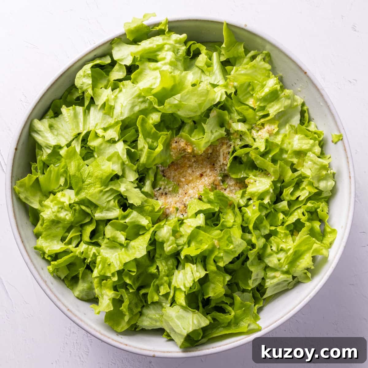 Toasted Garlic Salad with Crispy Garlic Dressing 8 Green chopped salad leaves with dressing in the middle in a pale grey bowl.