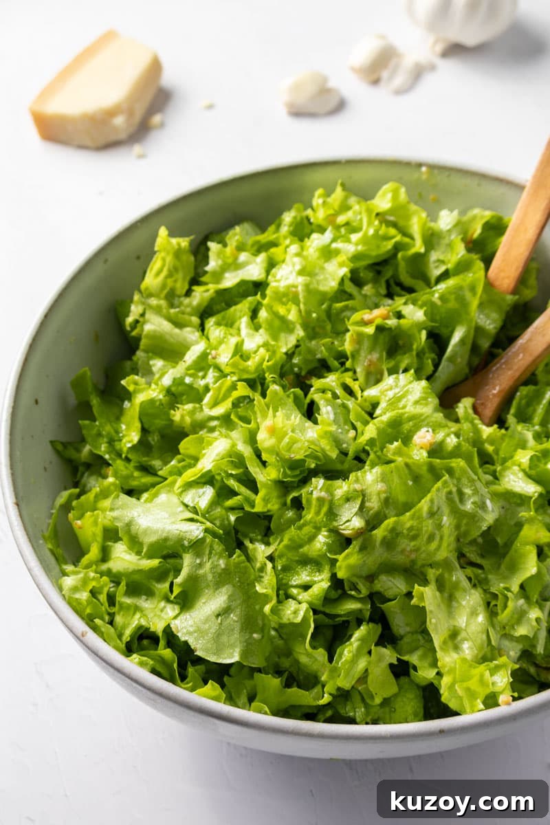 Toasted Garlic Salad with Crispy Garlic Dressing 10 A bowl of chopped dressed greens with two wooden spoons and garlic and parmesan in the background.