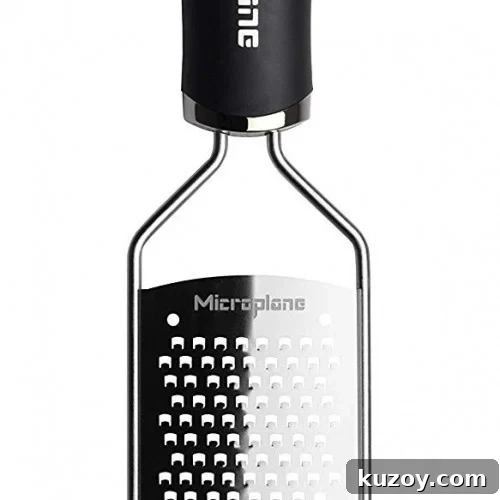 A stainless steel handheld grater with a black handle, featuring small, sharp holes for grating food. The word Microplane is visible on the graters surface.