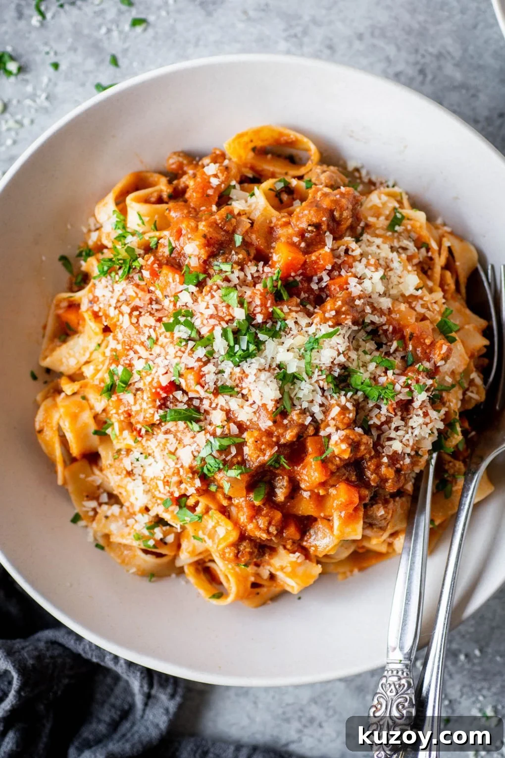 Pumpkin Ragu Pasta Sauce with Canned Pumpkin 3 Overhead & close up view of a large white bowl of fettuccine pasta with pumpkin ragu pasta sauce. It is topped with parmesan cheese and fresh parsley. There's a silver fork and spoon tucked into the bowl.