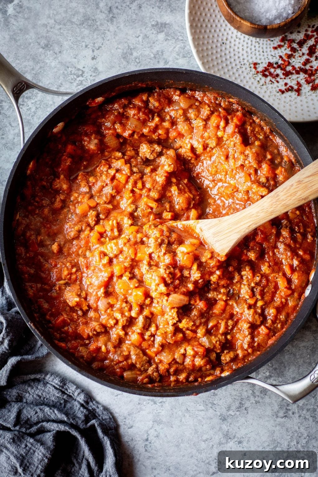 Pumpkin Ragu Pasta Sauce with Canned Pumpkin 5 Overhead shot of a skillet full of pumpkin ragu pasta sauce with a wooden spoon. On a dark grey background.