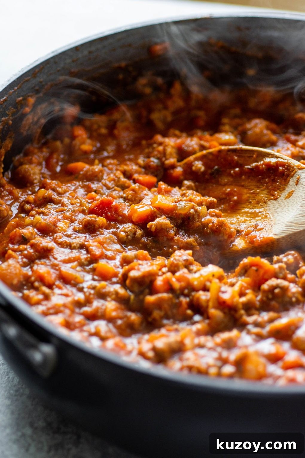 Pumpkin Ragu Pasta Sauce with Canned Pumpkin 8 Side angle view of a skillet of pumpkin ragu pasta sauce with a wooden spoon dipping into the steaming sauce.