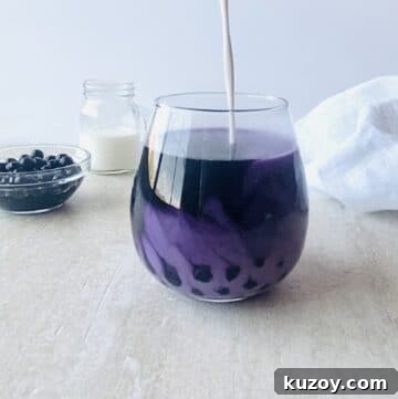 milk being poured into taro milk tea with boba in the background