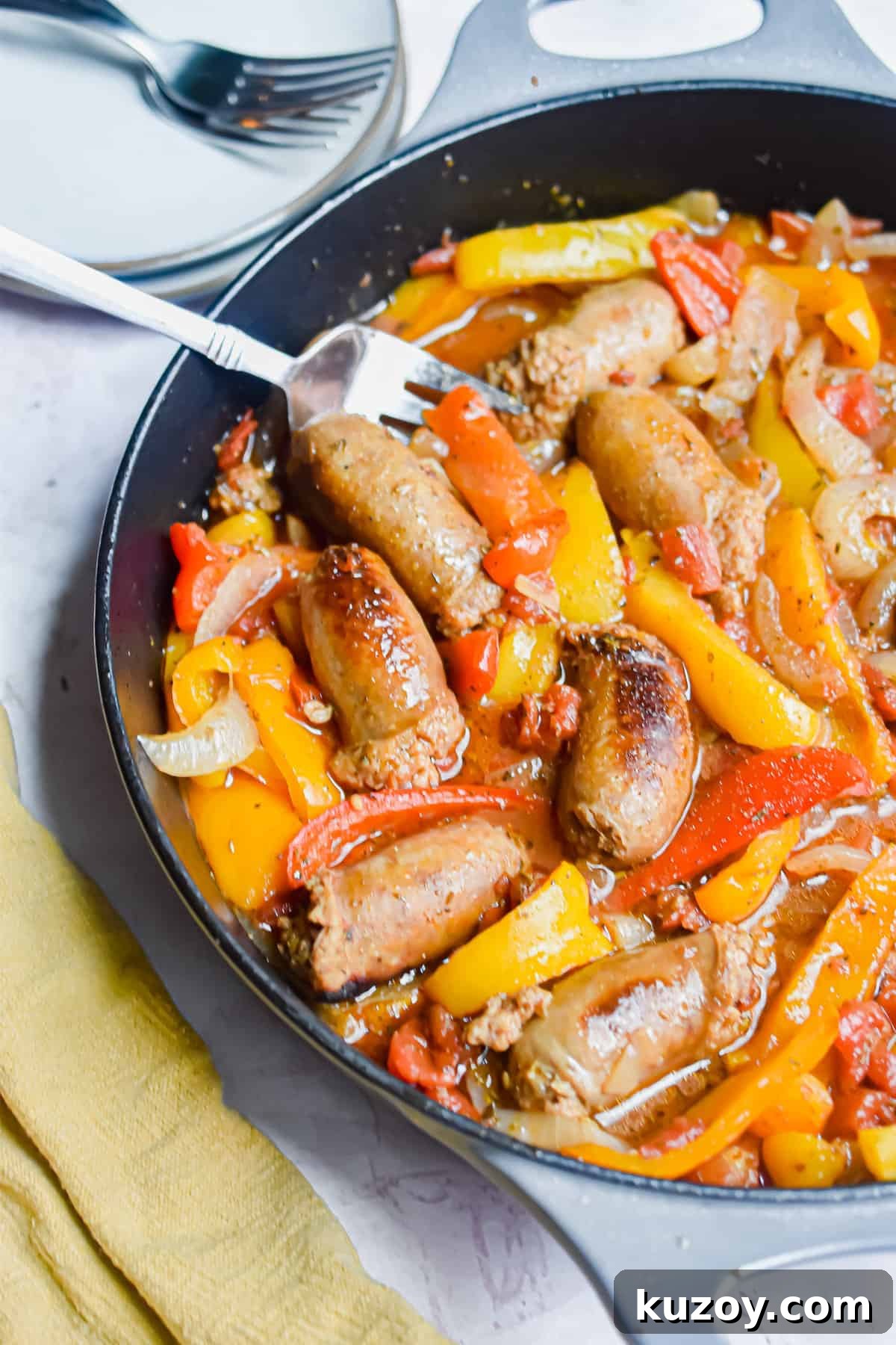 One-Pan Sausage and Peppers Recipe for Quick Weeknight Meals 2 A fork is in the pan with the one pot sausage and peppers and a yellow napkin on the corner of the pan.