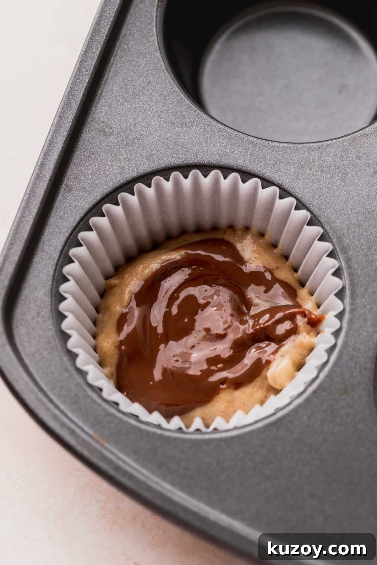 Nutella Banana Muffins Recipe — Gooey Chocolate Banana Muffins 7 Half of the batter in the muffin pan with Nutella on top.