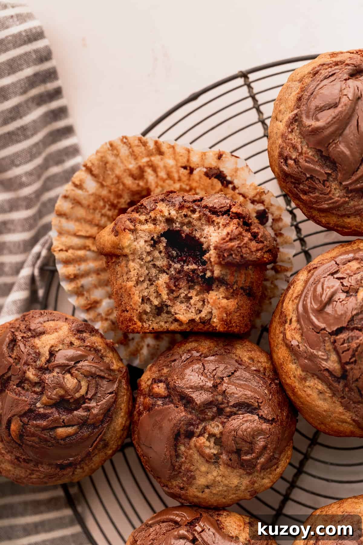 Nutella Banana Muffins Recipe — Gooey Chocolate Banana Muffins 10 Bite missing from a muffin on a wire rack.