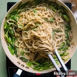 tossing spaghetti with tongs in a saute pan with asparagus