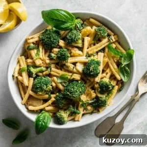 a ceramic bowl filled with tahini pasta and broccoli topped with basil on a marbled surface.