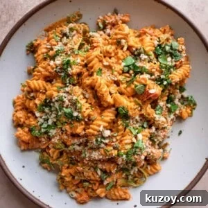 vegan roasted red pepper pasta salad in a speckled white bowl, garnished with basil.