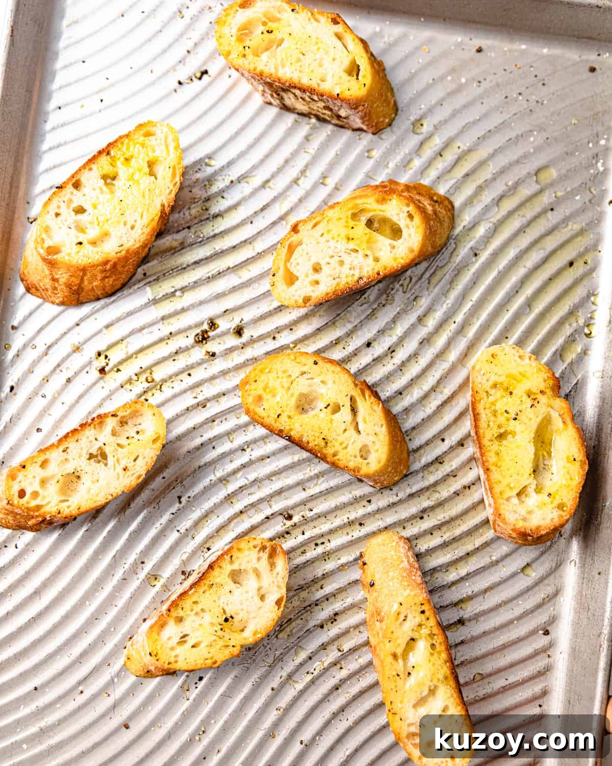 sliced bread on a baking sheet topped with olive oil, salt, and pepper.