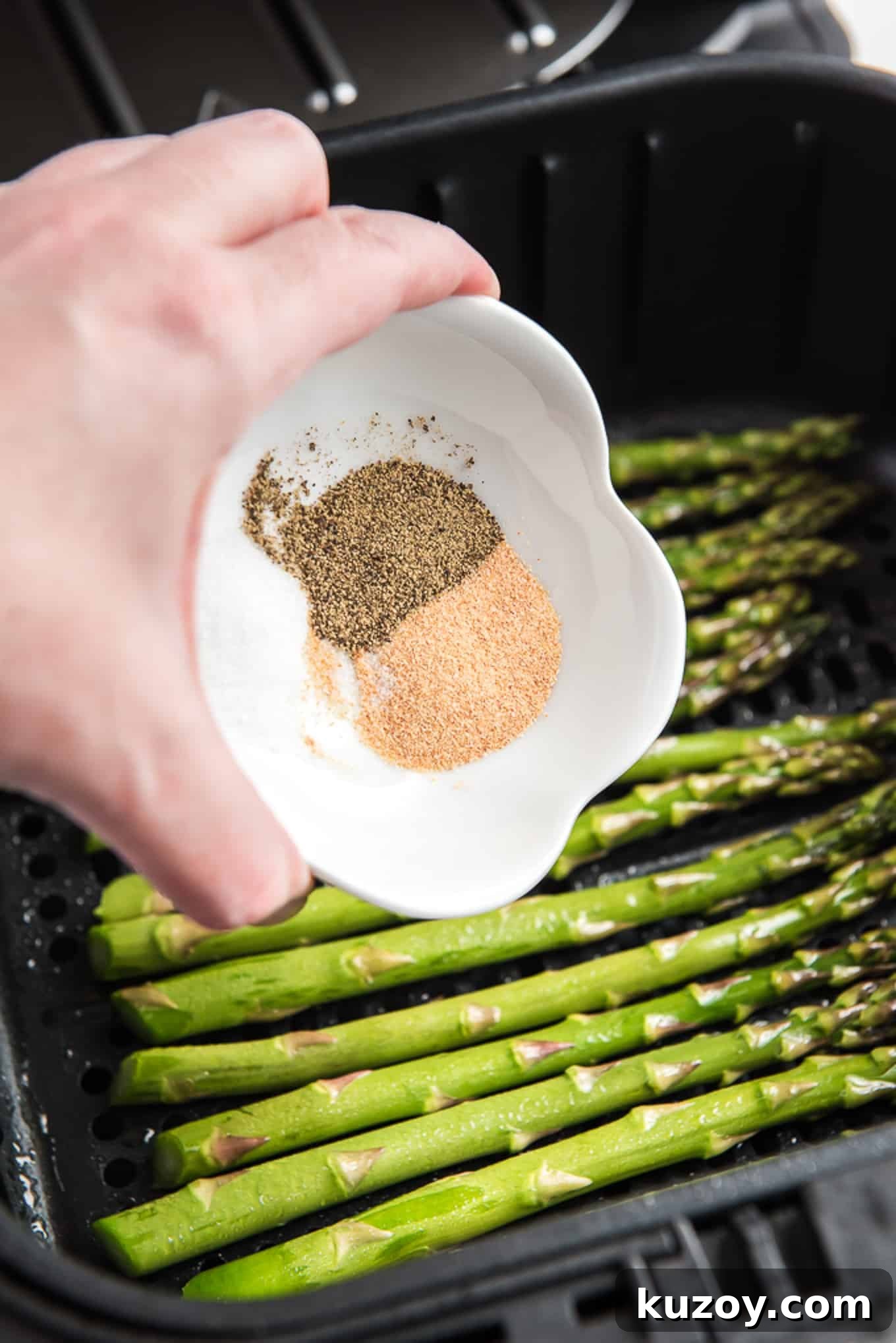 Crispy Air Fryer Asparagus Recipe with Garlic and Lemon 4 Pouring spices onto the prepared asparagus in the air fryer basket.