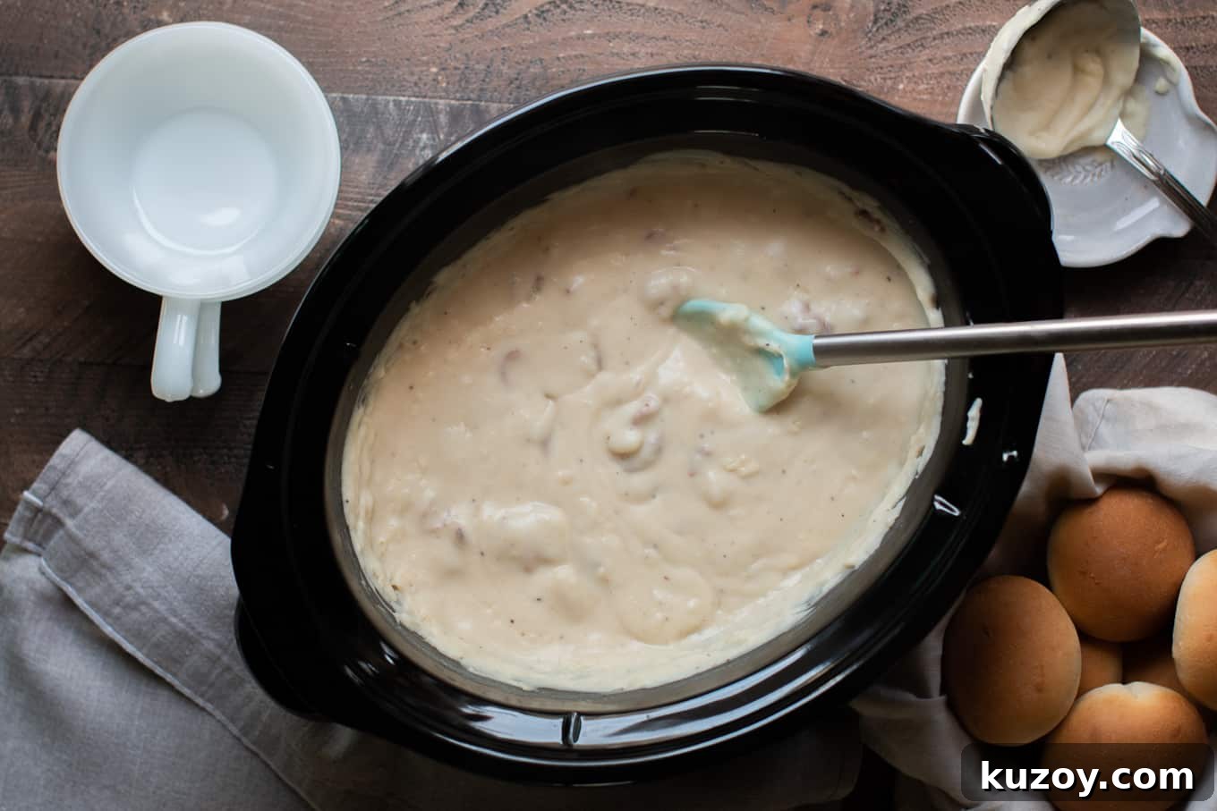 Creamy Slow Cooker Potato and Bacon Soup Recipe 3 creamy blended potato soup in a slow cooker with bowls and rolls on the side.