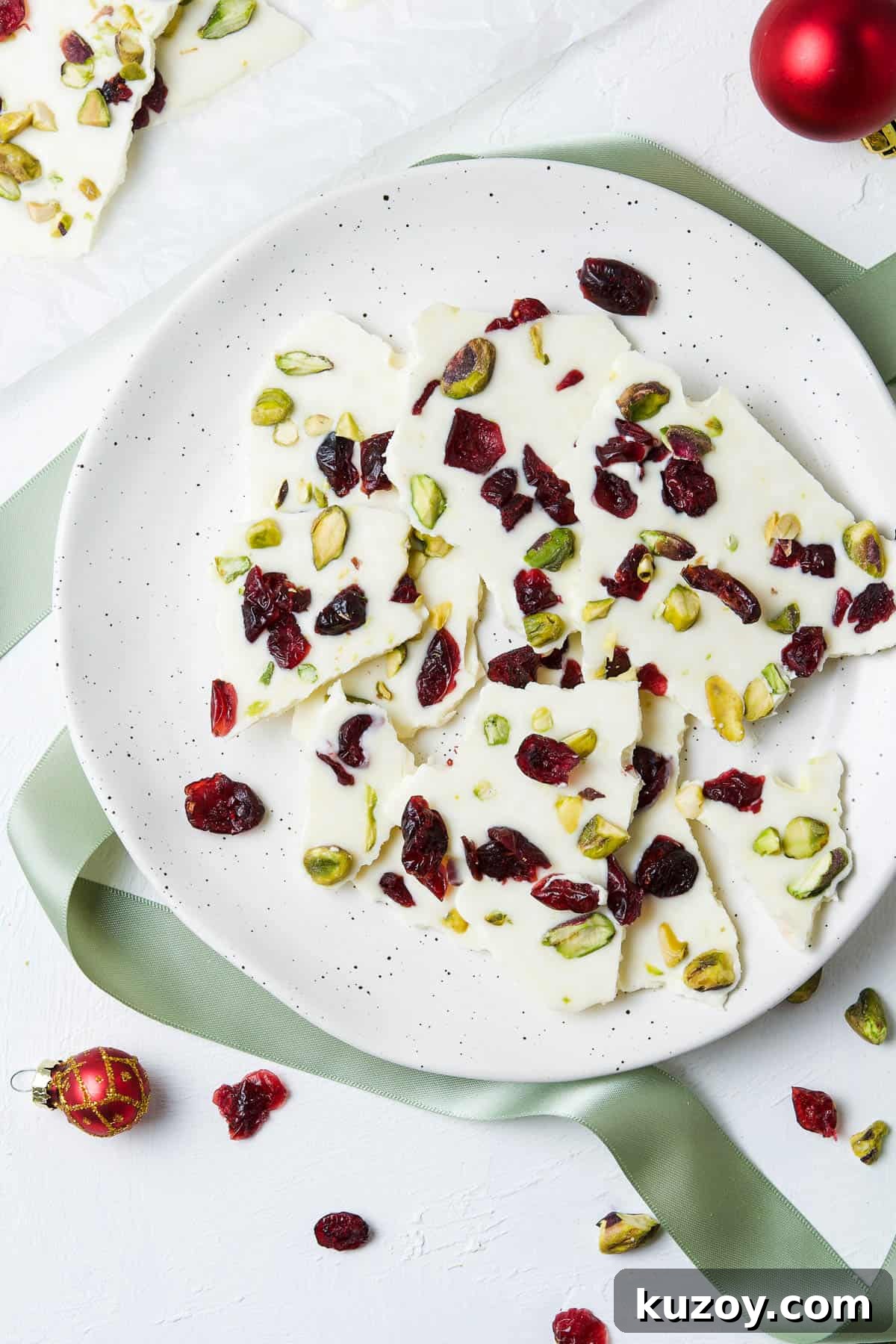 Cranberry Pistachio Chocolate Bark Recipe for Holiday Gifts 2 round plate with bark, surrounded by some cranberries and decorations.