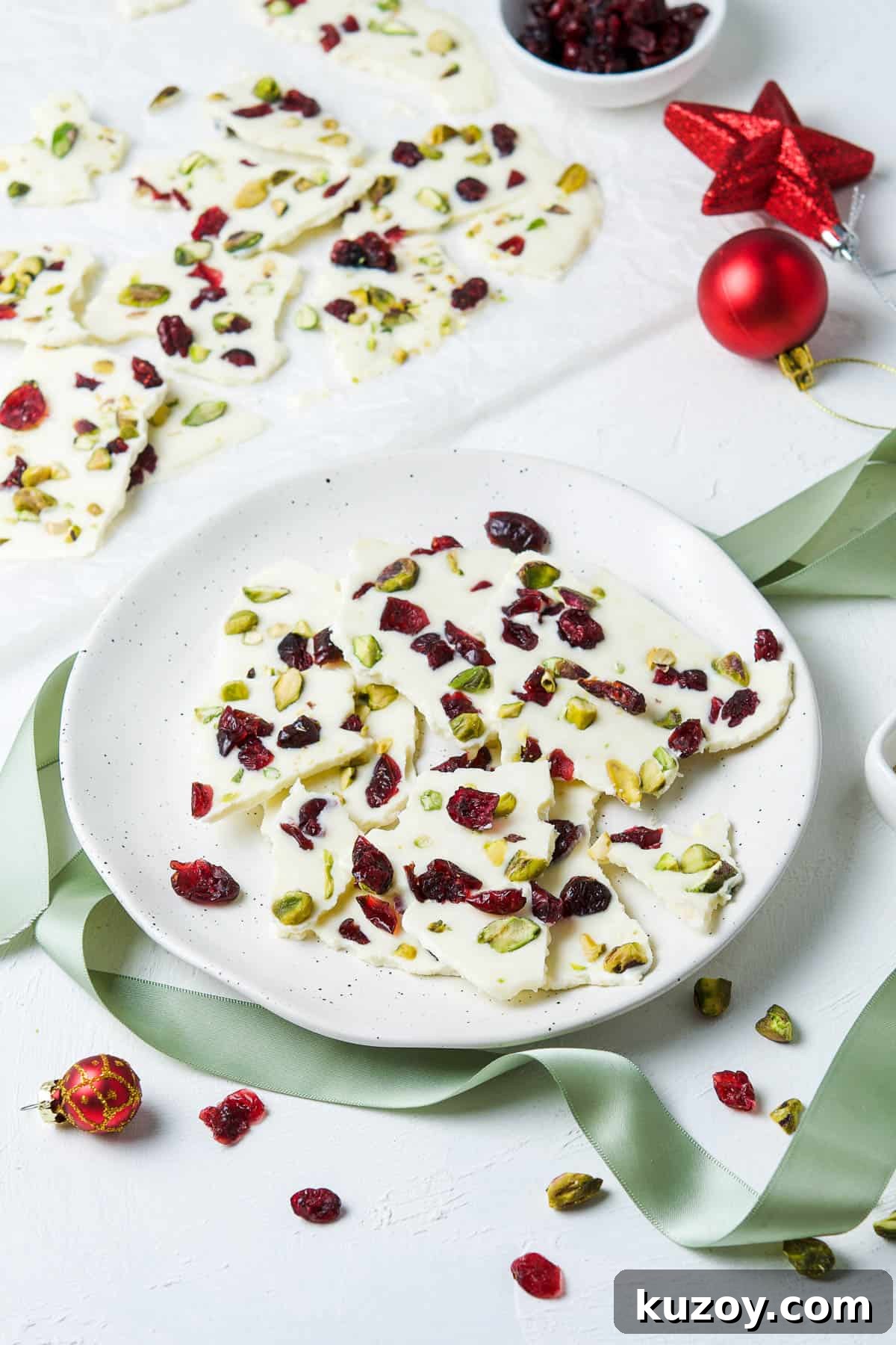 Cranberry Pistachio Chocolate Bark Recipe for Holiday Gifts 6 round plate of bark, with more bark in the background, and some decorations around the plate.