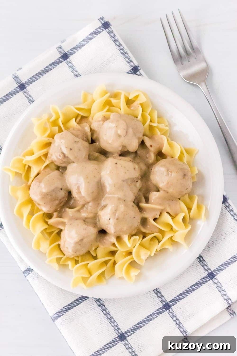 Instant Pot Swedish Meatballs Recipe: Creamy Sauce in 30 Minutes 3 overhead view of a white plate serving egg noodles topped with pressure cooker Swedish meatballs, and a fork off to the side