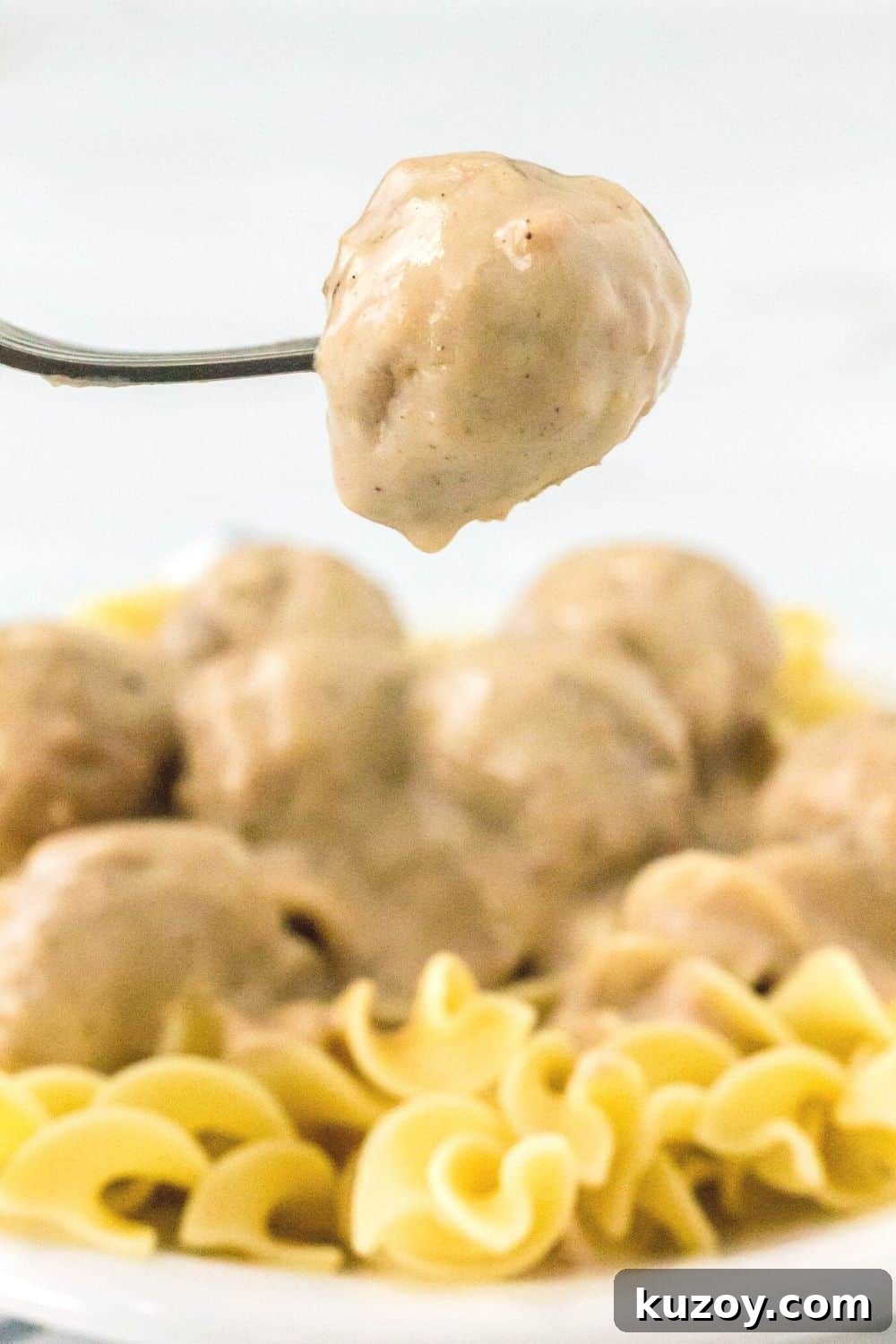 Instant Pot Swedish Meatballs Recipe: Creamy Sauce in 30 Minutes 4 a fork holds a Swedish meatball suspended over a bed of egg noodles and more meatballs that were cooked in the Instant Pot